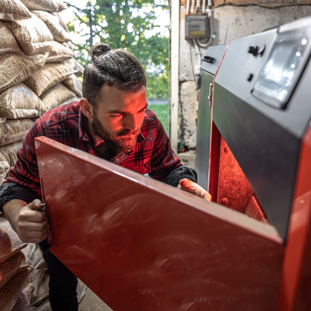 A man looking into a boiler on solid fuel, open door boiler with flames of fire.